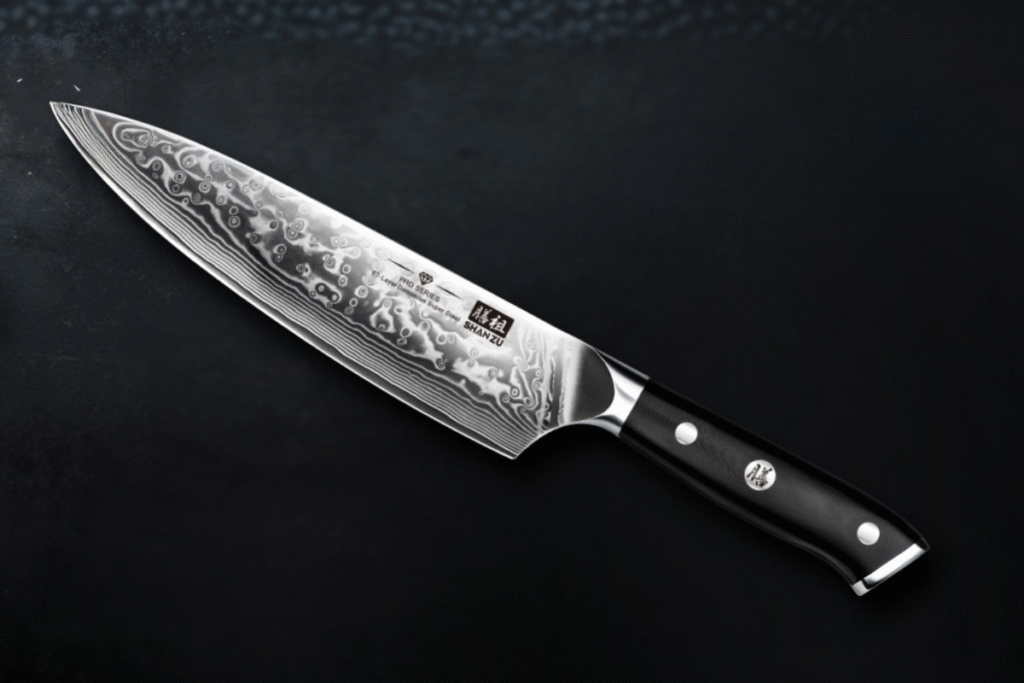 Cuchillo japonés SHAN ZU de acero Damasco con hoja de 67 capas y mango negro ergonómico, sobre fondo oscuro
