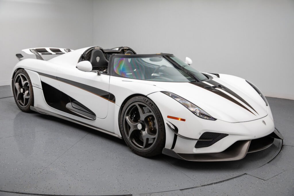 Vista lateral del Koenigsegg Regera 2019 en blanco perla con detalles en negro y dorado, mostrando su silueta agresiva y techo desmontable.