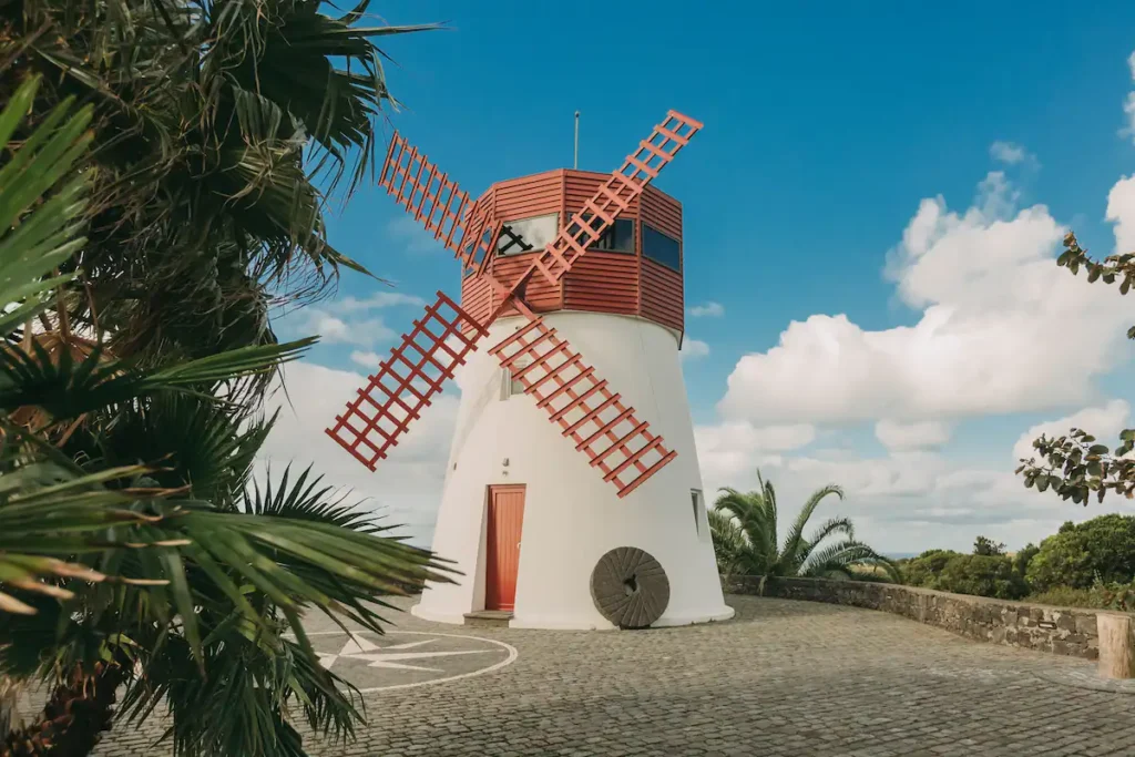 Molino de viento restaurado con aspas rojas en Azores, rodeado de vegetación tropical