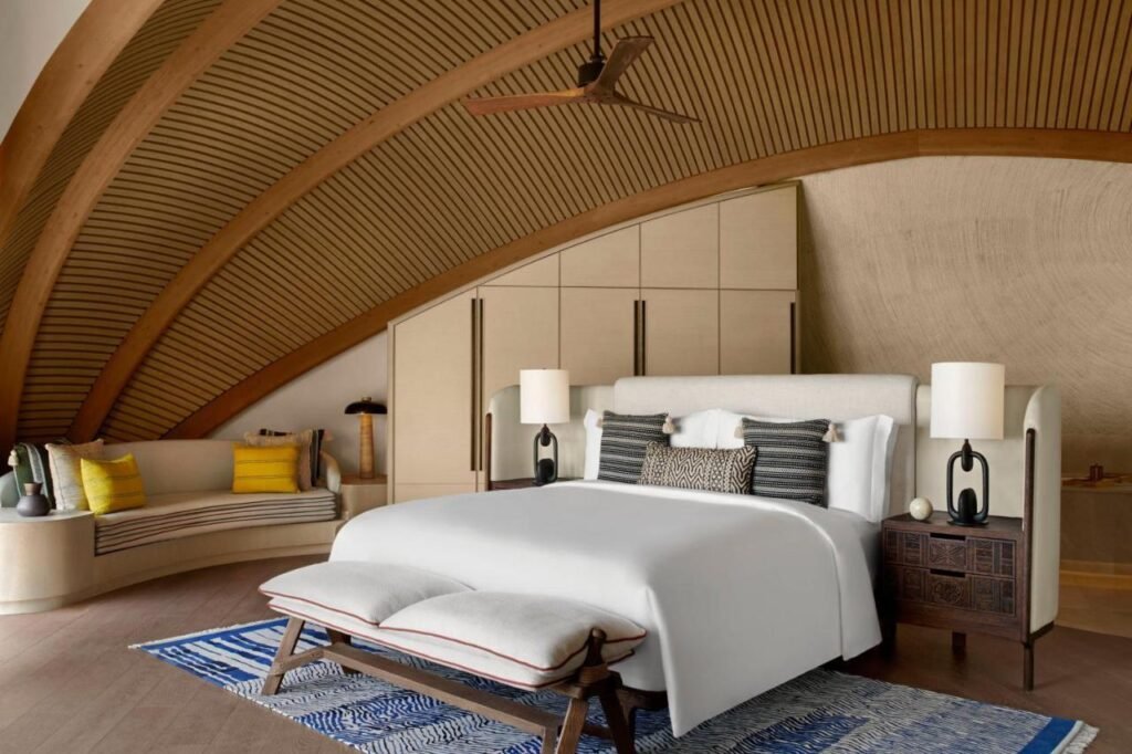Dormitorio elegante y espacioso en una de las villas del hotel Nujuma, con diseño curvo de madera y decoración natural.