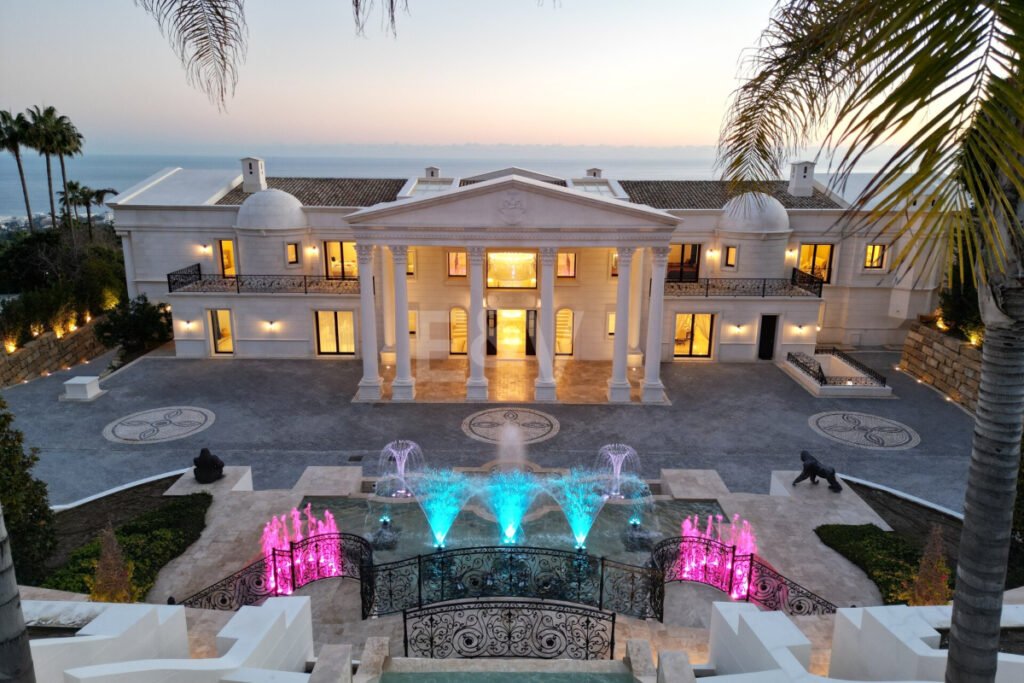 Entrada principal de Villa Bellagio al atardecer, con fuentes iluminadas y vistas al mar Mediterráneo.