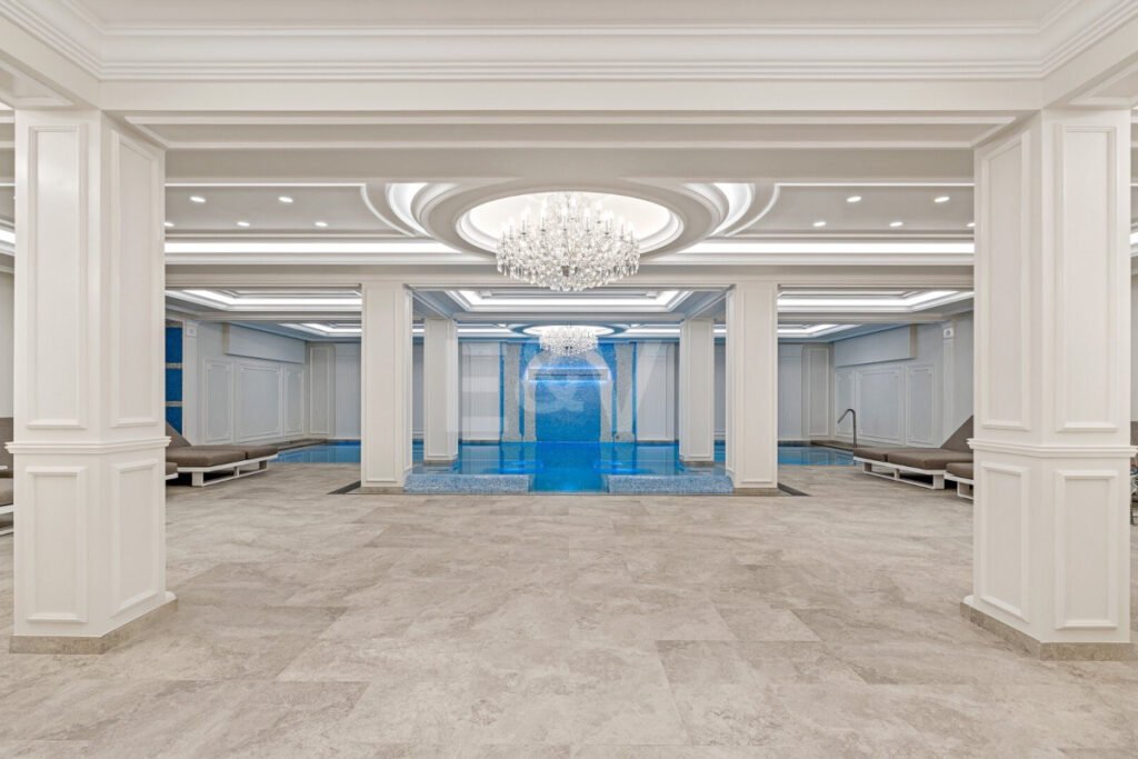 Piscina interior climatizada en Villa Bellagio con cascada decorativa, columnas clásicas y candelabros de cristal.
