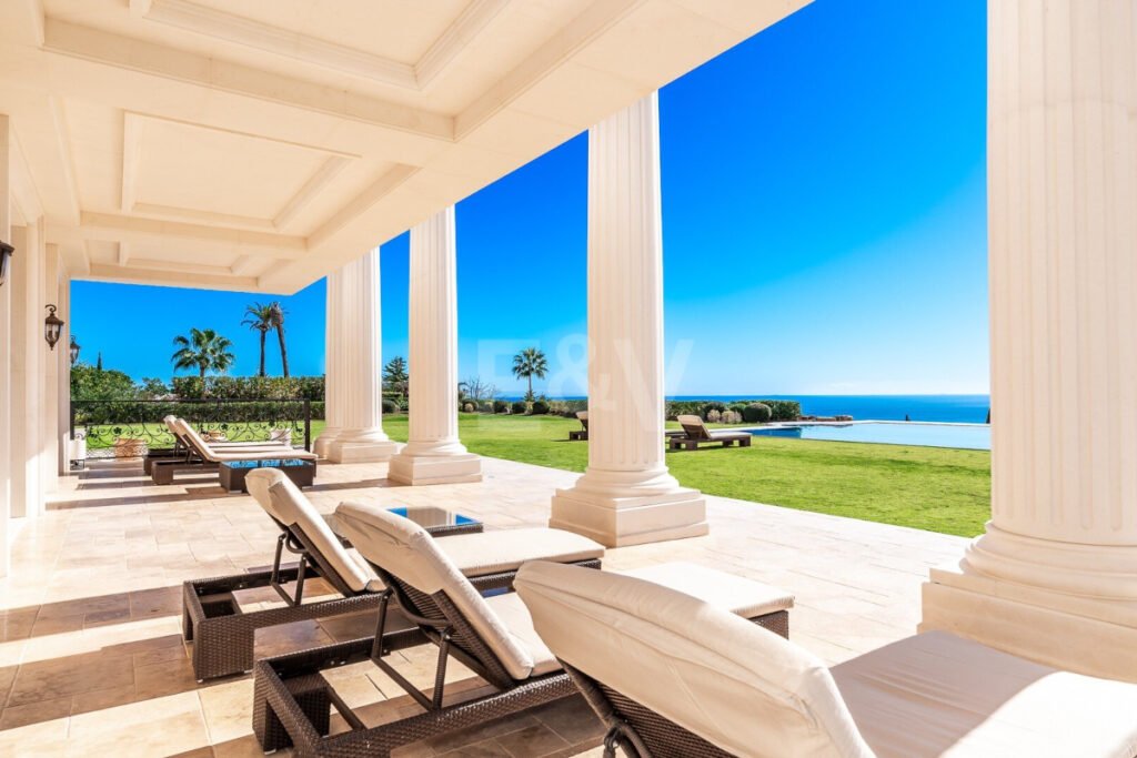 Terraza cubierta con columnas clásicas y vistas al mar desde las tumbonas junto a la piscina infinity en Villa Bellagio.