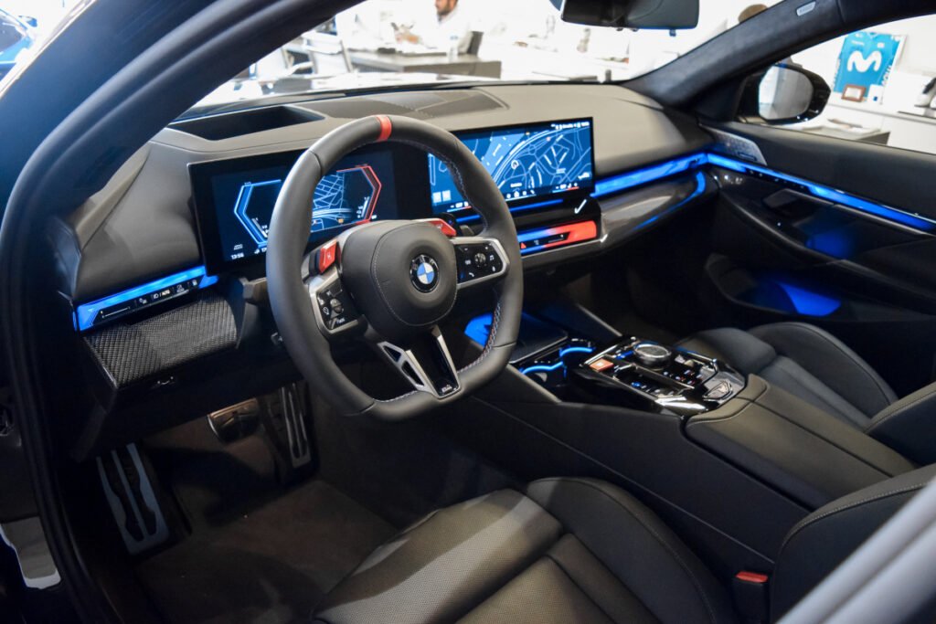 Puesto de conducción del BMW M5 con doble pantalla curva, volante M y ambiente tecnológico.