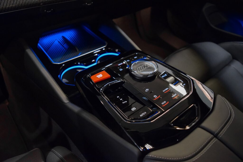 Plano cenital de la consola central del BMW M5 con selector M, mandos táctiles y botón rojo de arranque.