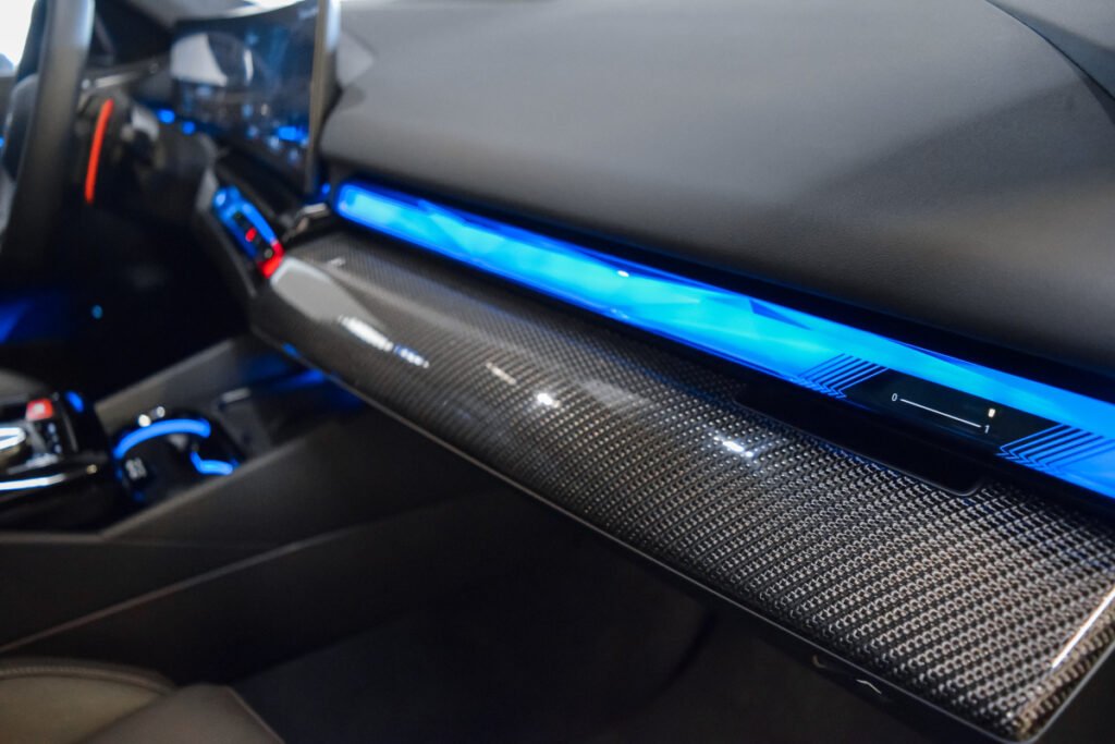 Detalle del salpicadero del BMW M5 con moldura de carbono y luz ambiental azul.